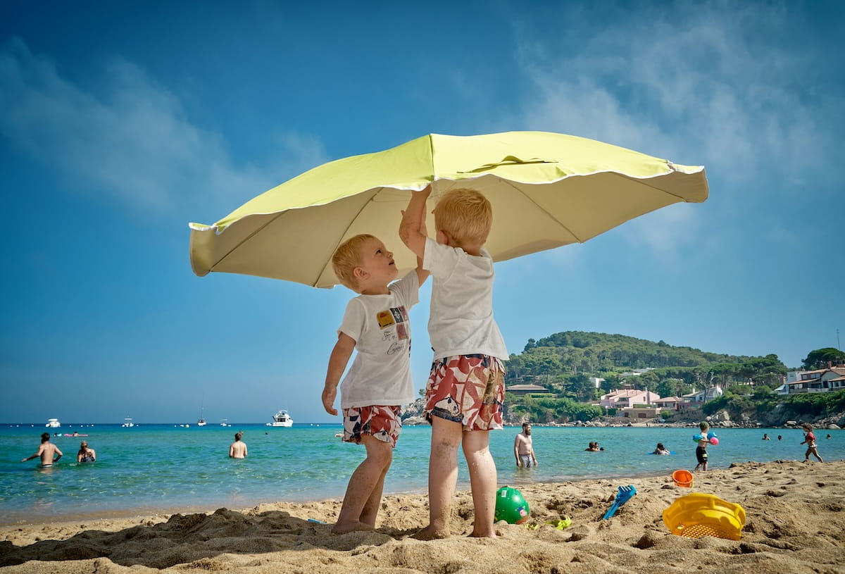 Kinder spielen unter Sonnenschirm an familienfreundlichem Sandstrand mit flachem Wasser auf Mallorca
